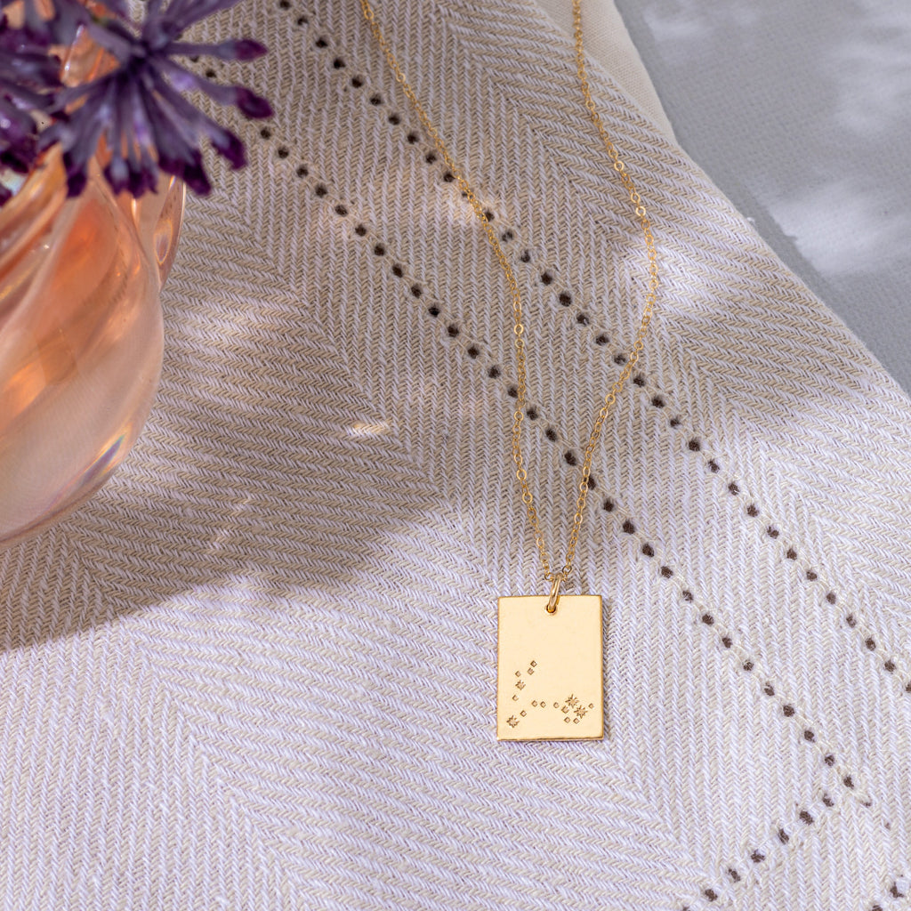 a gold necklace with a small square pendant